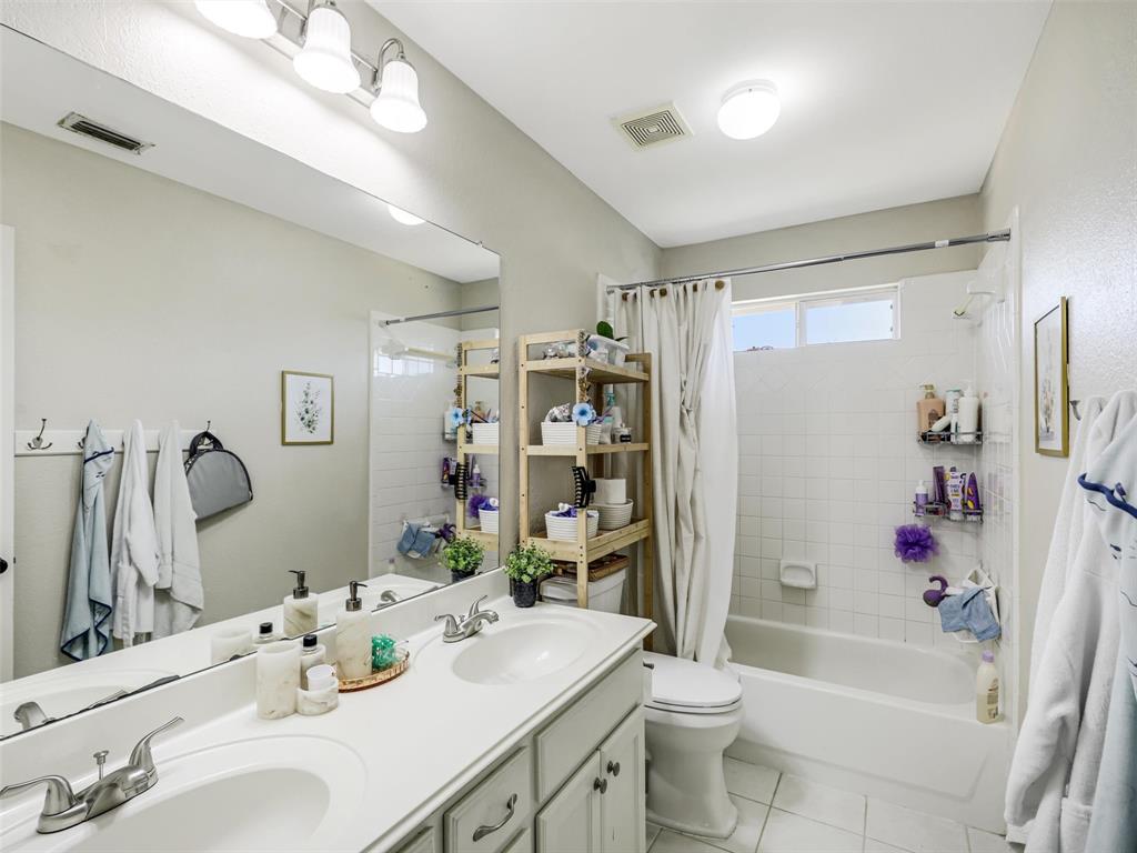 Dual vanity with integrated sinks, full-width mirror, white tile flooring, and a tub-shower combination with white subway tile surround