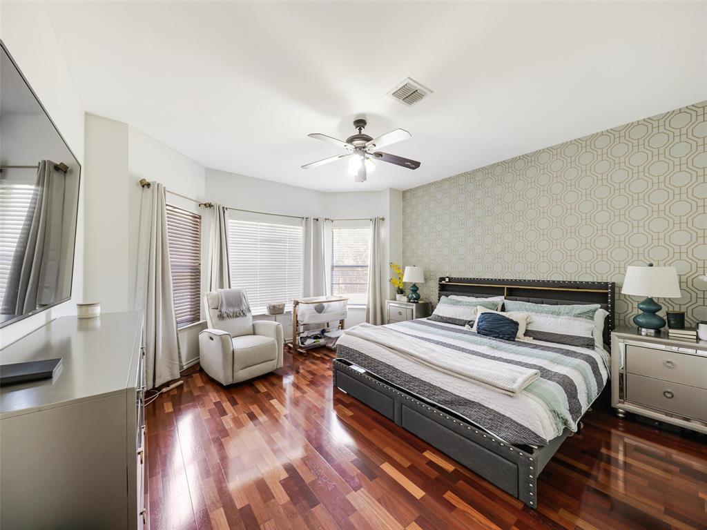 Hardwood flooring, bay window with blinds, ceiling fan, and accent wall