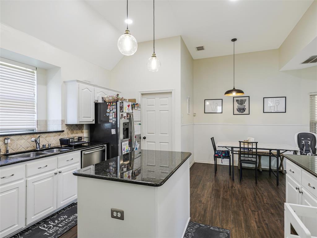 Kitchen featuring white cabinetry, dark countertops, wood-finish flooring, a center island, and a tile backsplash Kitchen featuring white cabinetry, dark countertops, wood-finish flooring, a center island, and a tile backsplash