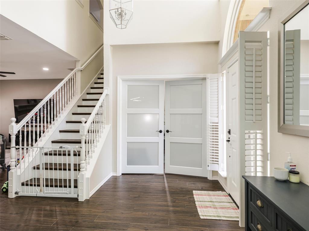 Two-story entry with wood-finish flooring, a white spindle staircase with dark treads, and a modern chandelier Two-story entry with wood-finish flooring, a white spindle staircase with dark treads, and a modern chandelier