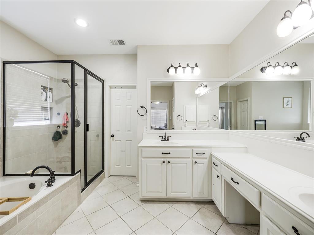 Black-framed glass shower enclosure, built-in soaking tub with black fixtures, dual white vanity with integrated sinks, expansive wall-mounted mirror, and tile flooring