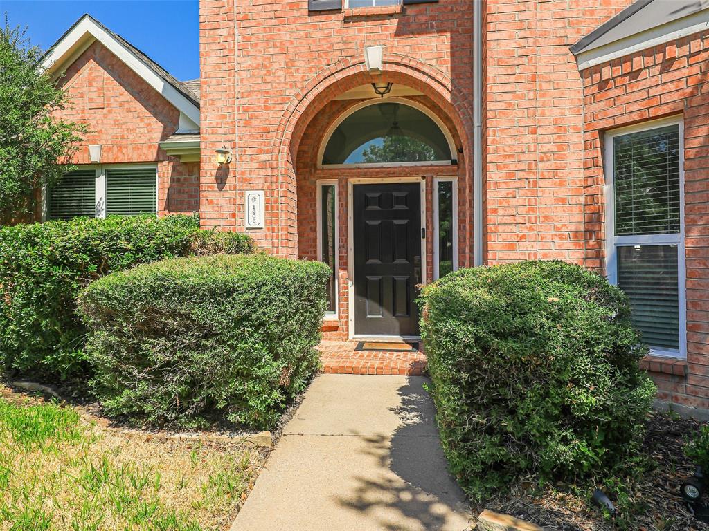 Brick exterior with arched entryway, black paneled door, and established shrubbery Brick exterior with arched entryway, black paneled door, and established shrubbery