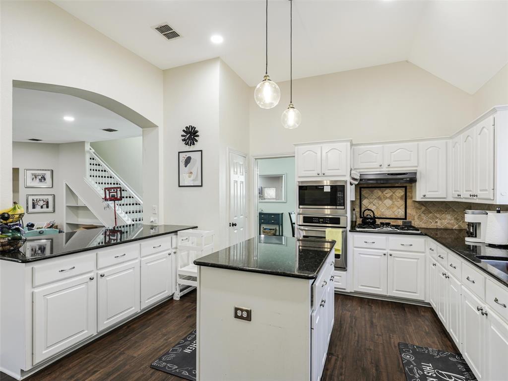 Kitchen featuring white cabinetry, dark countertops, wood-finish flooring, stainless steel appliances, and a vaulted ceiling