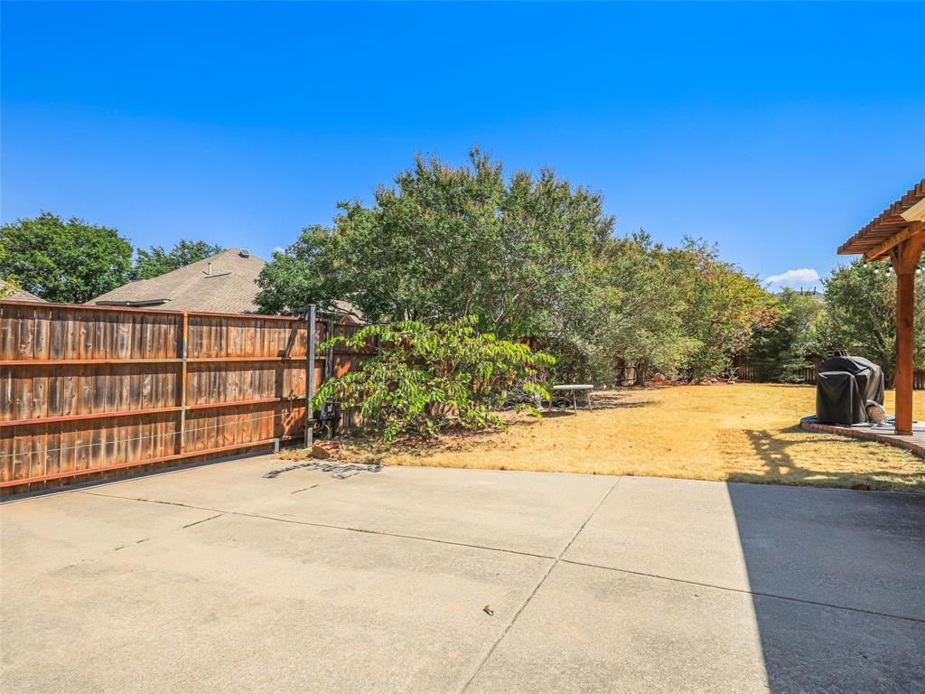 Expansive backyard with a concrete patio, wood fence, and mature trees
