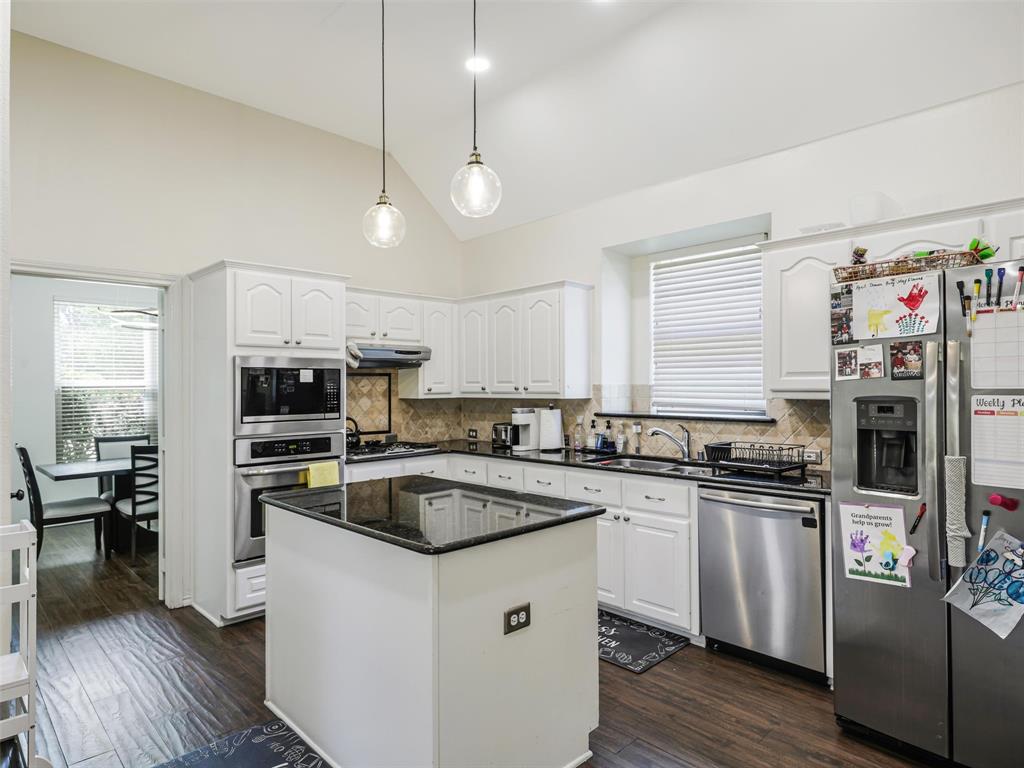 Kitchen featuring vaulted ceilings, white cabinetry, a center island with a dark countertop, stainless steel appliances, and wood-finish flooring