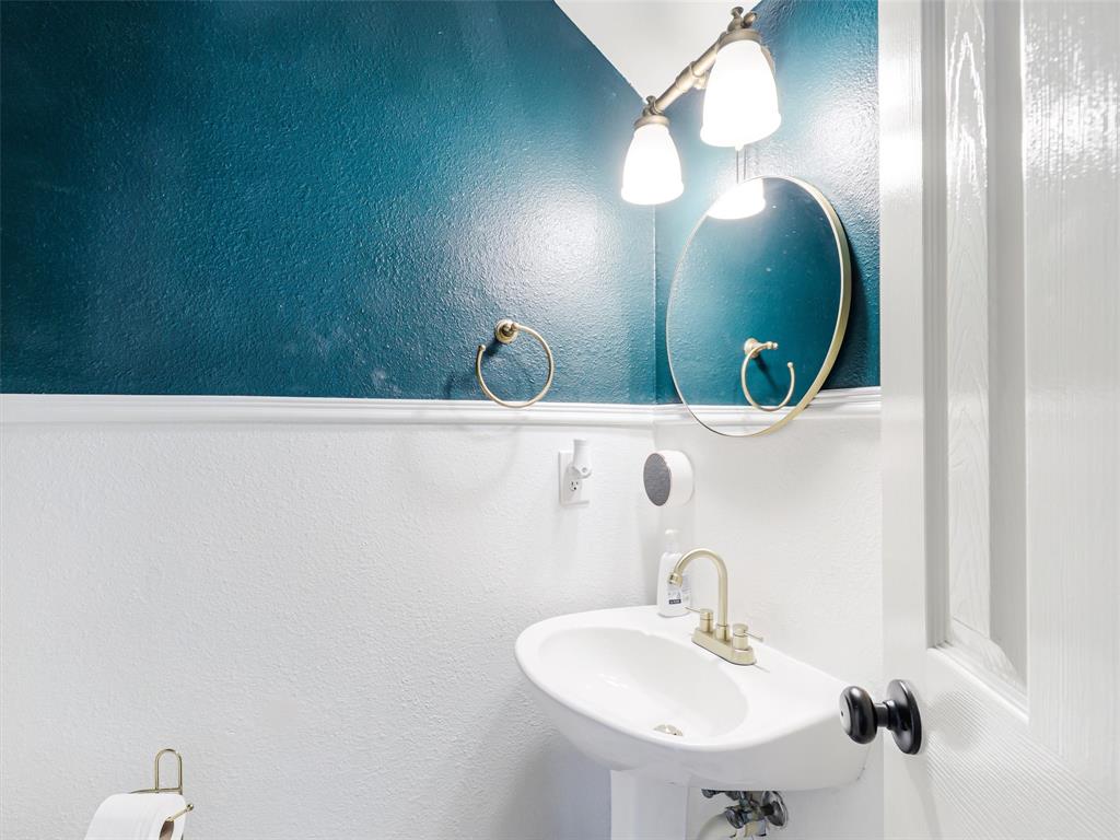Pedestal sink with brass-finish faucet, circular mirror, and wall-mounted vanity light