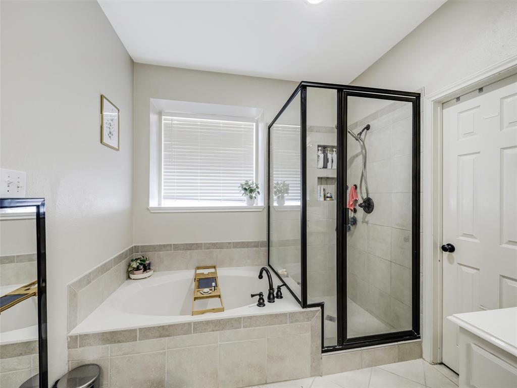 Built-in soaking tub with tiled surround, separate glass-enclosed shower with tiled walls, and window with blinds