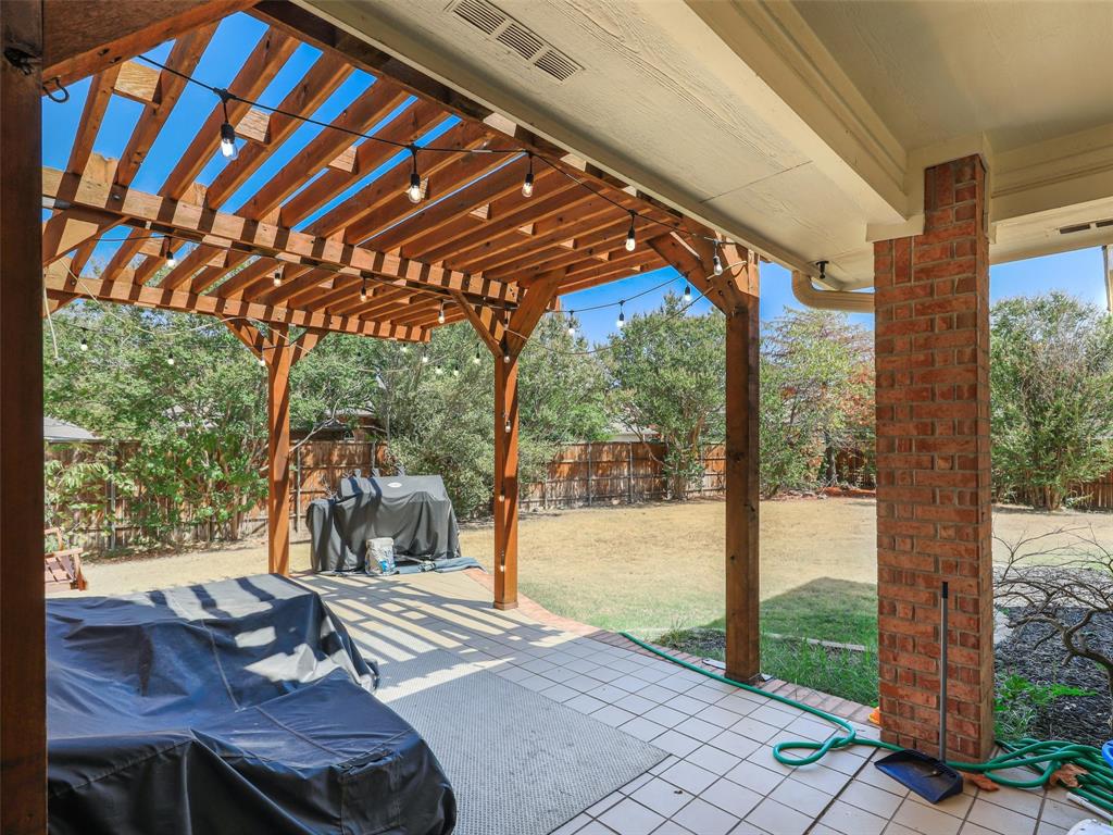 Expansive outdoor living area featuring a wood pergola with string lights, brick column accents, and a tiled patio surface