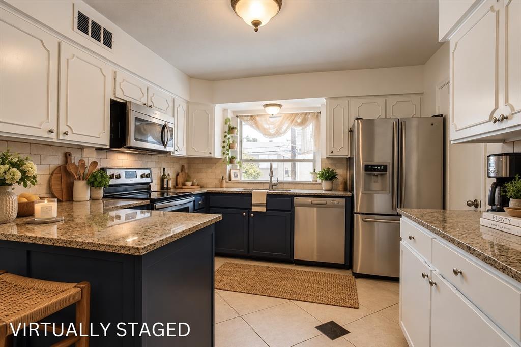 Kitchen featuring granite countertops, stainless steel appliances, white upper cabinetry, dark lower cabinetry, and light-toned tile flooring