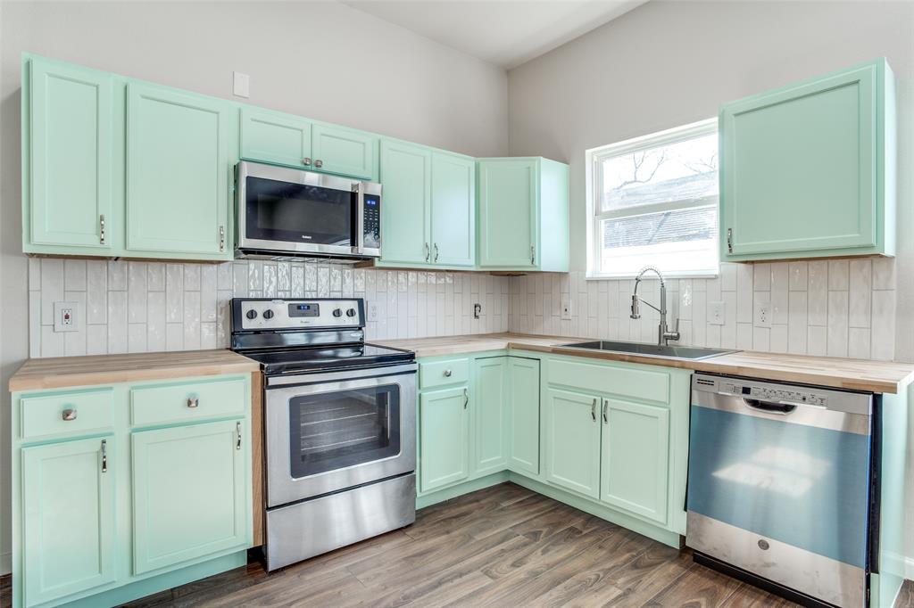 Kitchen featuring decorative backsplash, a sink, wood counters, appliances with stainless steel finishes, and wood finished floors