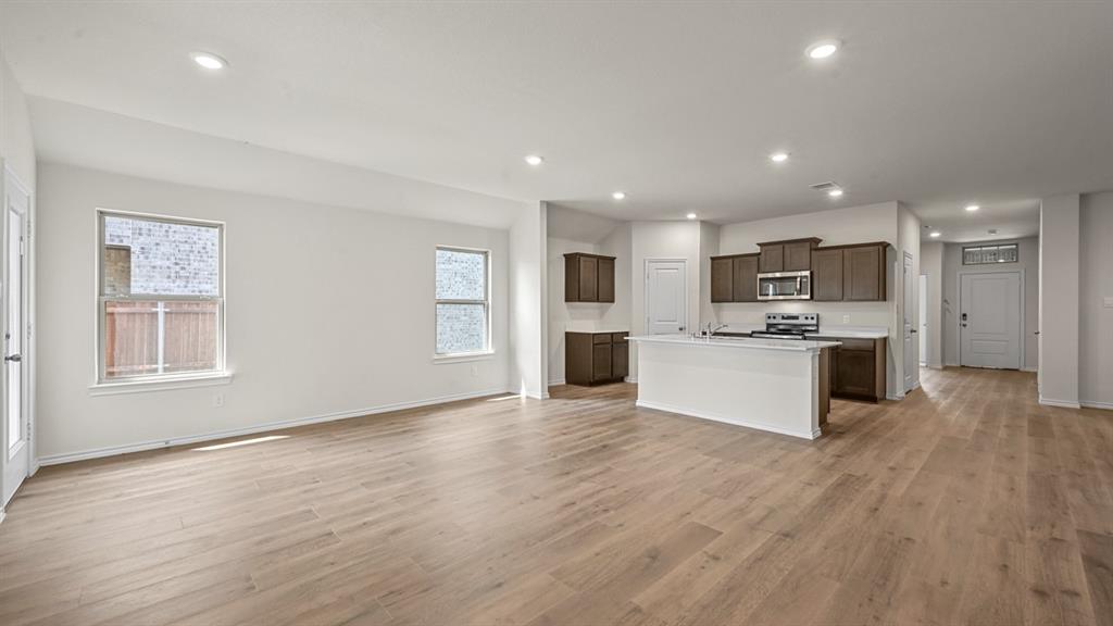 Wood-finish flooring throughout, recessed ceiling lighting, kitchen island with built-in sink, stainless steel appliances, and dark wood-finish cabinetry