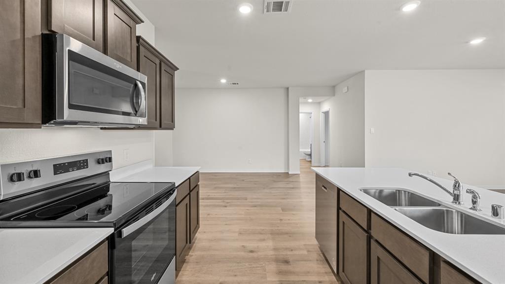 Contemporary kitchen featuring stainless steel appliances, dark wood cabinetry, white countertops, a double basin sink, and wood-finish flooring