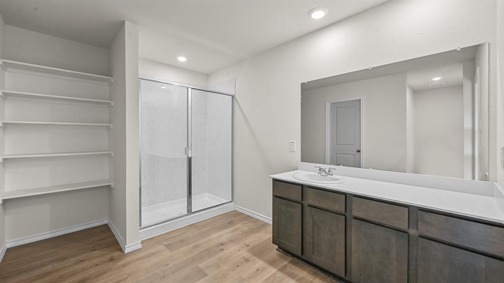 Wood-finish flooring, built-in shelving, glass-enclosed shower, dual-sink vanity, and expansive wall mirror