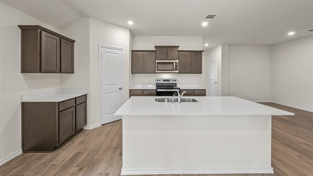 Open-concept kitchen featuring an island with a stainless steel sink, wood-finish flooring, dark wood cabinetry, and stainless steel appliances