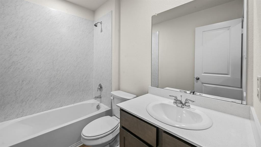 Bathroom featuring a white tub and shower combination with textured wall surround, a toilet, a vanity with a drop-in sink, and a large wall-mounted mirror