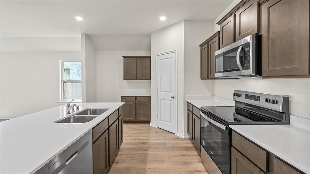 Kitchen featuring wood-finish flooring, stainless steel appliances, white countertops, and dark wood cabinetry