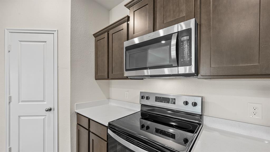 Stainless steel microwave, coordinating stainless steel electric range, white countertops, and wood-finish cabinetry
