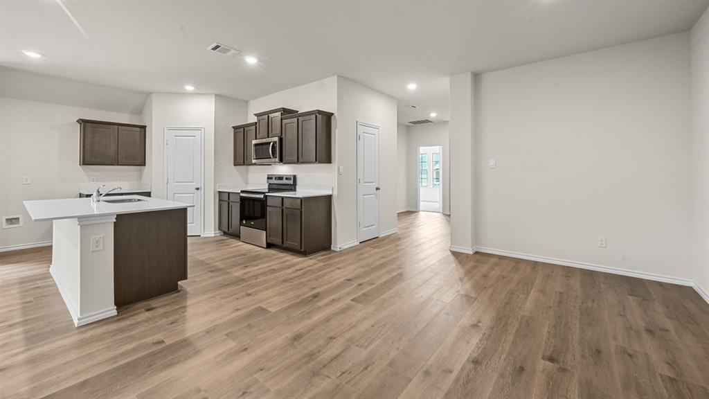 Wood-finish flooring throughout, kitchen island with a light-toned countertop, dark wood-tone cabinetry, stainless steel range, and recessed lighting