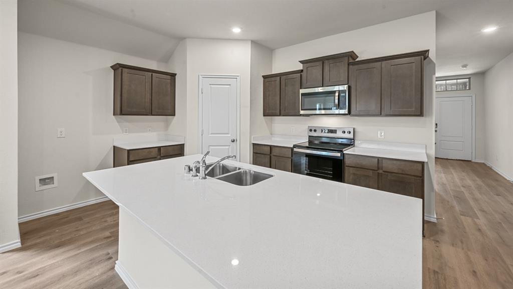 Kitchen featuring a large island with a stainless steel double sink, white countertops, dark wood-finish cabinetry, and wood-finish flooring