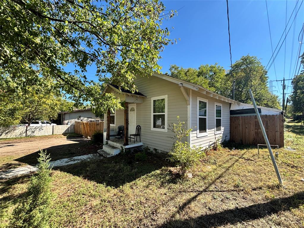 Single-story residence featuring light-toned horizontal siding, a covered front porch with wood-finished support columns, and a perimeter wood-fencing enclosure