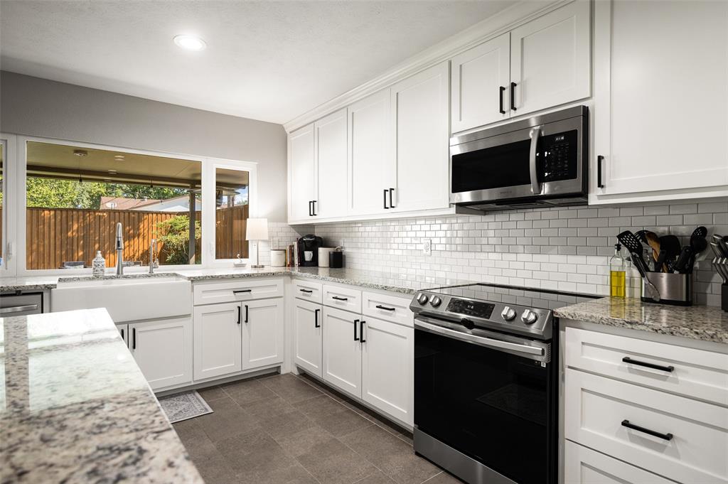 White shaker cabinetry with matte black hardware, stainless steel appliances, subway tile backsplash, light-toned stone countertops, and an undermount farmhouse sink