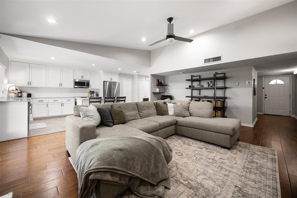 Vaulted ceiling with a ceiling fan, recessed lighting, wood-finish flooring, white cabinetry, and stainless steel appliances