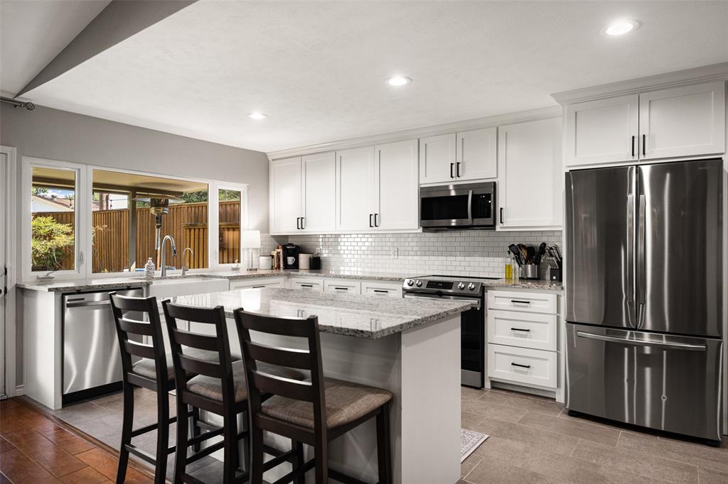 Modern kitchen featuring white shaker cabinetry, stainless steel appliances, a center island with countertop seating, and a subway tile backsplash