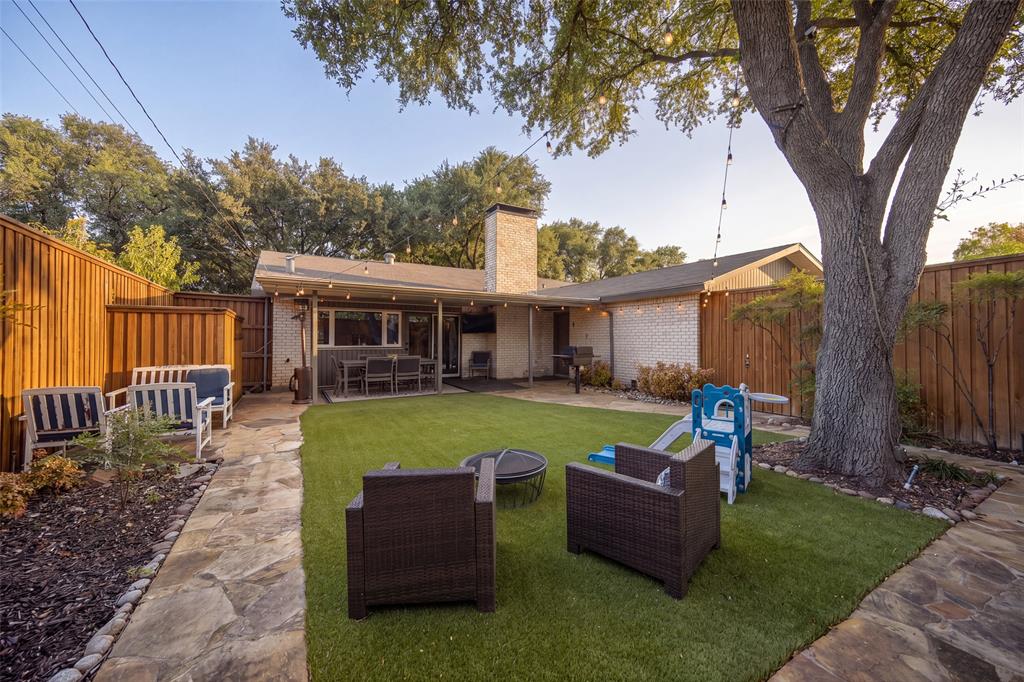 Manicured backyard featuring a stone patio, artificial turf, a mature tree, and privacy fencing