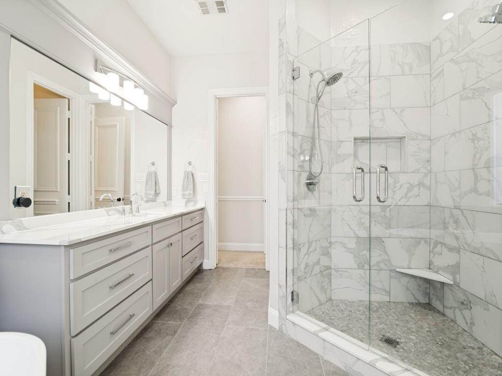 Beautiful master bath renovation completed in 2023 features separate vanities and oversized glass and tiled shower.