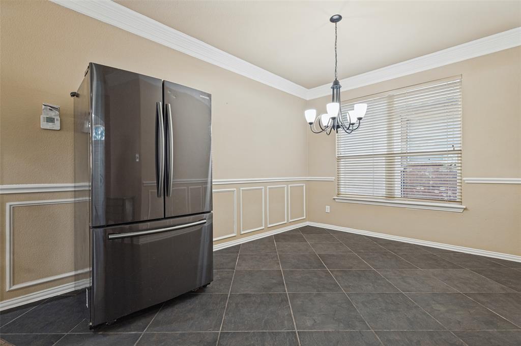 Spacious room featuring dark large-format tile flooring, decorative wainscoting, crown molding, and an overhead chandelier light fixture