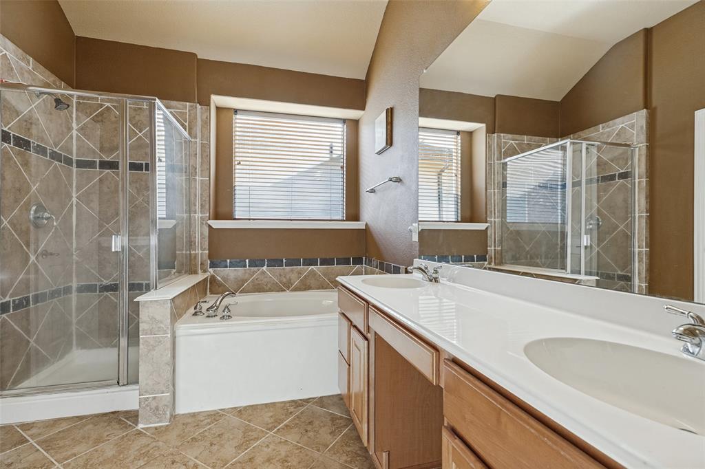 Beautifully tiled bath with dual vanity with dual sinks, a tiled shower with glass enclosure, a white soaking tub, and tile flooring