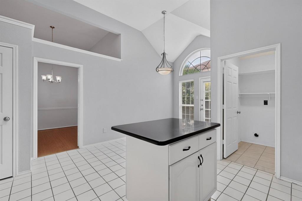 Vaulted ceiling with an arched window, white tile flooring, white cabinetry island with black countertop, and an exterior door with integrated blinds