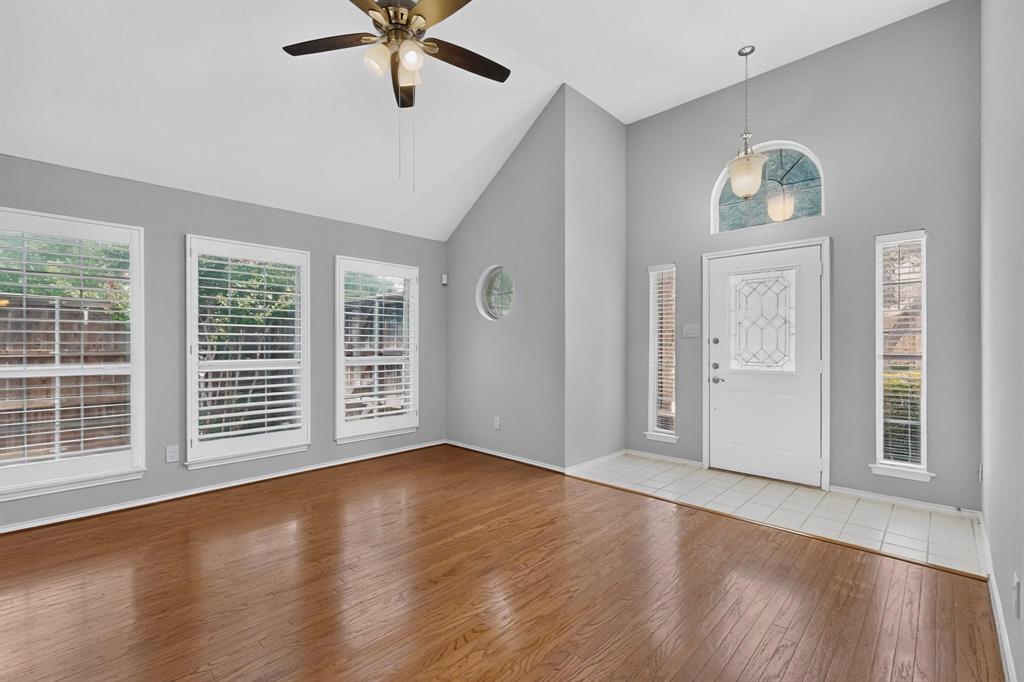 Vaulted ceiling with a ceiling fan, wood-finish flooring, multiple windows with plantation shutters, white entry door with decorative glass, and a tiled entry area