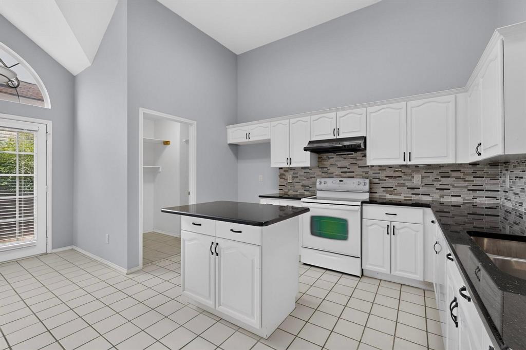 Kitchen featuring vaulted ceilings, white cabinetry, dark countertops, a tiled backsplash, and a central island