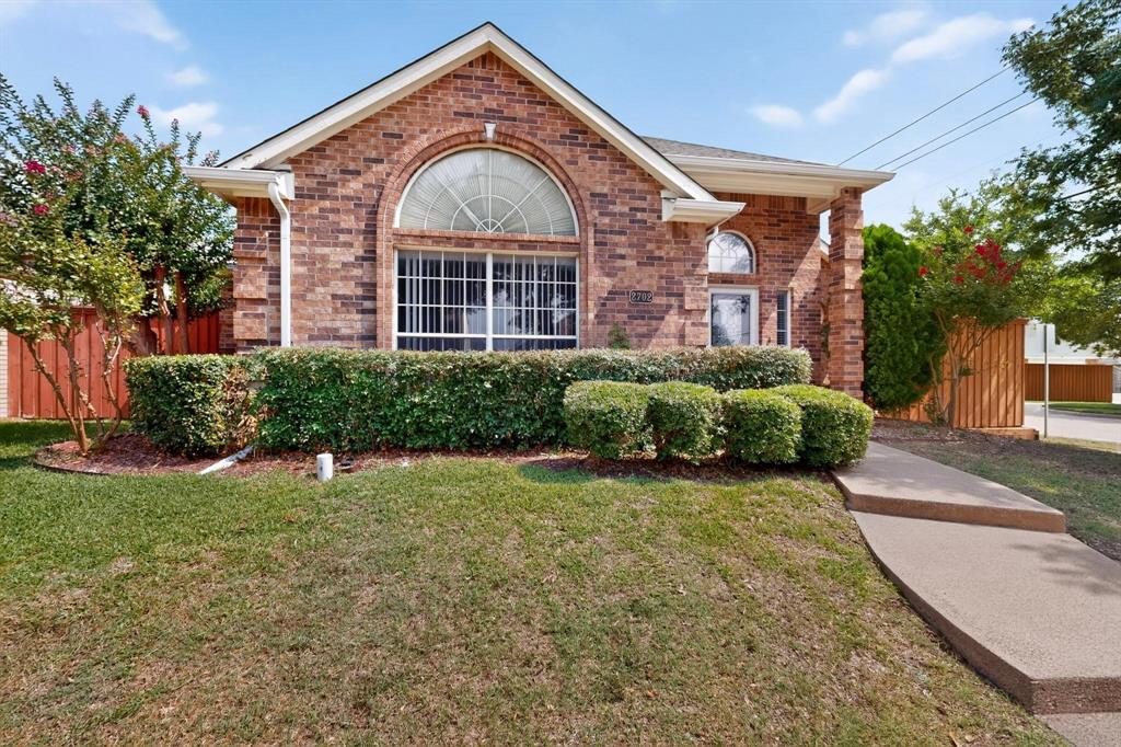 Brick exterior with an arched window, a covered entryway, and mature landscaping