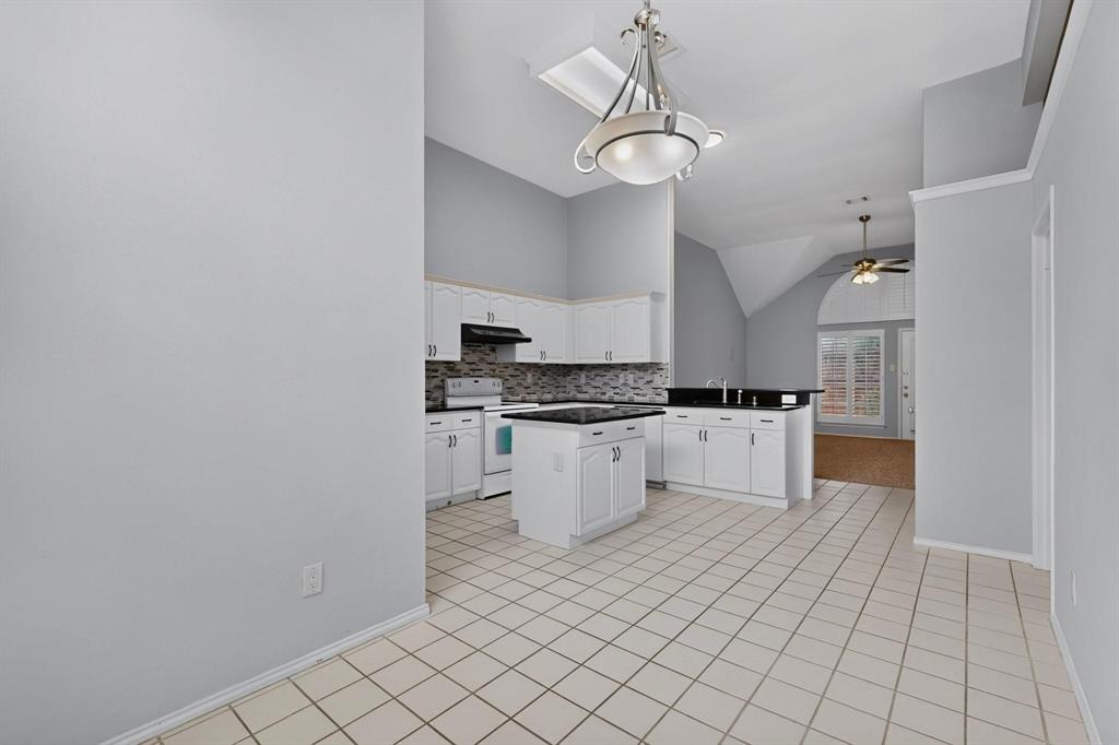 Kitchen featuring white cabinetry, dark countertops, a mosaic tile backsplash, a center island, and tile flooring