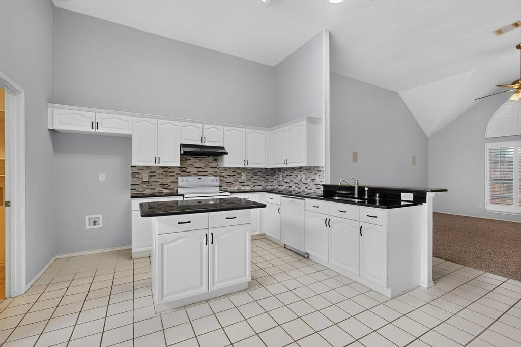 Kitchen featuring white cabinetry, black countertops, a central island, and a tiled backsplash