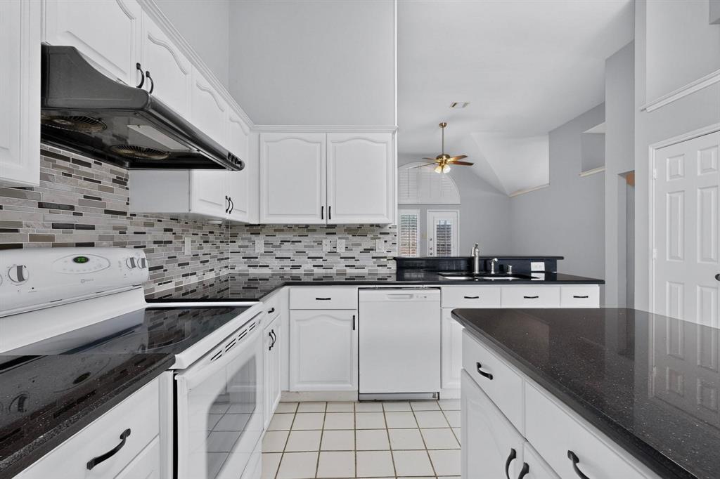 Kitchen featuring white cabinetry, black countertops, tile flooring, a tile backsplash, and white appliances