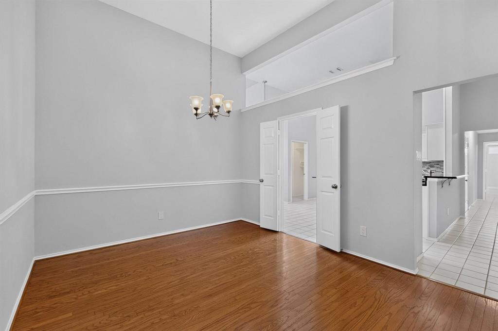 Vaulted ceiling with an attached chandelier, wood-finish flooring, wainscoting, and white bi-fold doors