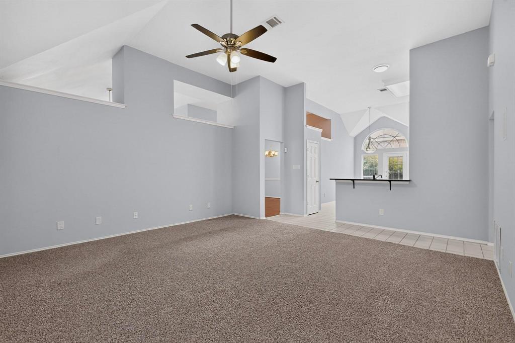 Vaulted ceilings, contemporary ceiling fan, carpet flooring, a breakfast bar with an overhanging countertop, and a tiled entry