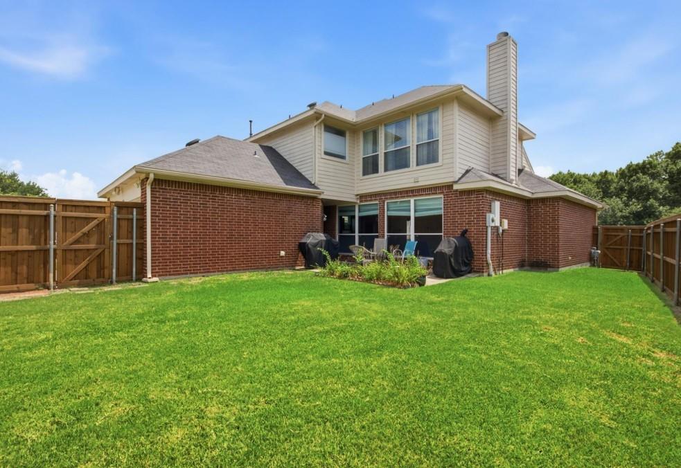 Expansive green lawn, brick and siding exterior, multi-pane windows, and a paved patio area