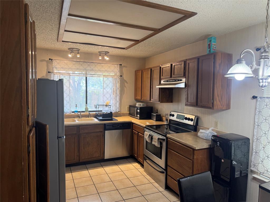 Kitchen featuring wood cabinetry, tiled flooring, stainless steel refrigerator, and ample counter space