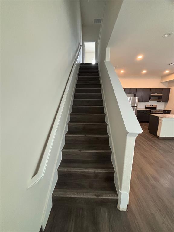 Staircase featuring wood-finish treads and risers, a white handrail, and white newel posts