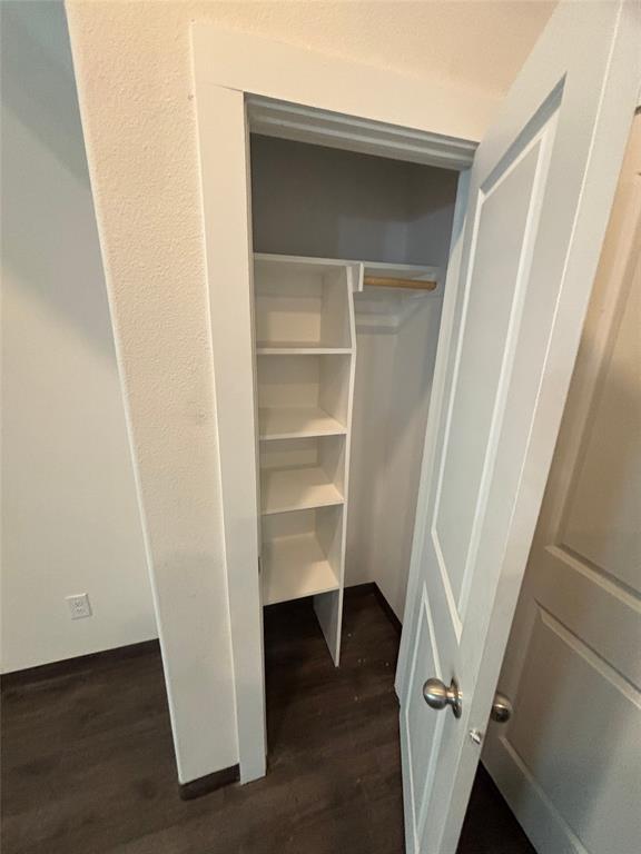 Built-in shelving, hanging rod, wood-finish flooring, white panel door, and brushed nickel door hardware