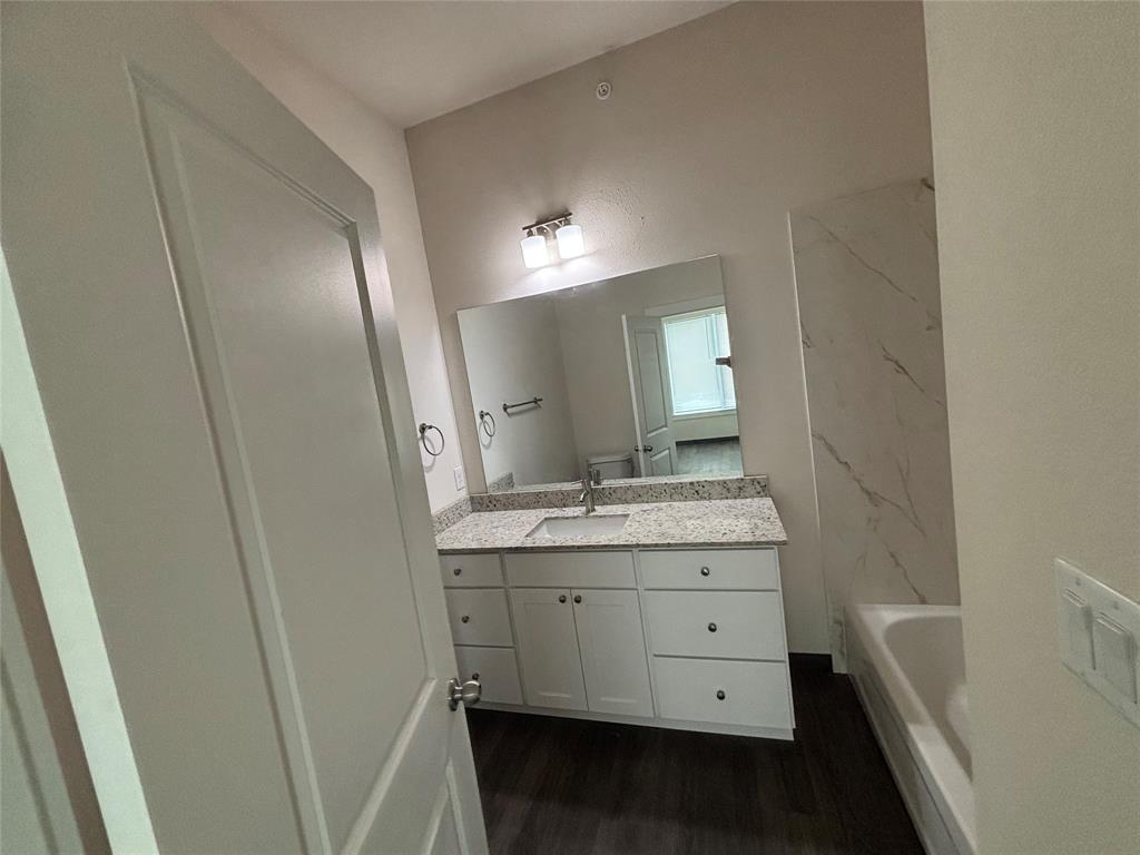 Bathroom featuring a single vanity with stone-finish countertop, white cabinetry, undermount sink, and wood-finish flooring