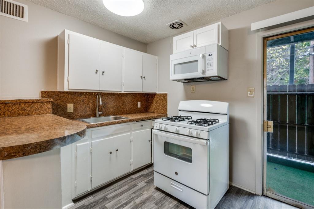 Kitchen featuring white cabinetry, brown granite-look countertops, stainless steel sink, wood-finish flooring, and a built-in microwave