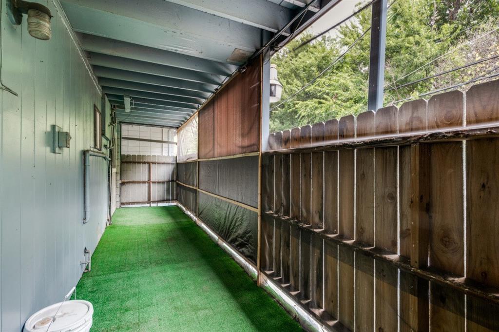 Covered outdoor area featuring synthetic turf flooring, wooden privacy fencing, and exposed beam ceiling