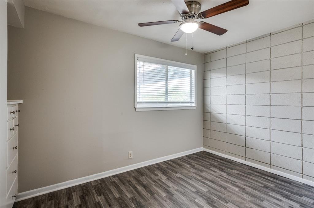 Wood-finish flooring, accent wall featuring rectangular paneling, window with horizontal blinds, built-in cabinetry with drawer pulls, and a ceiling fan with integrated lighting