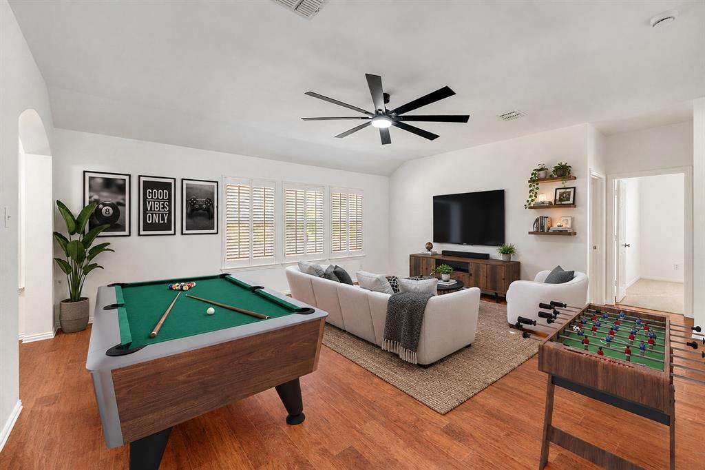 Spacious living area featuring wood-finish flooring, multiple windows with plantation shutters, a ceiling fan, and built-in floating shelves