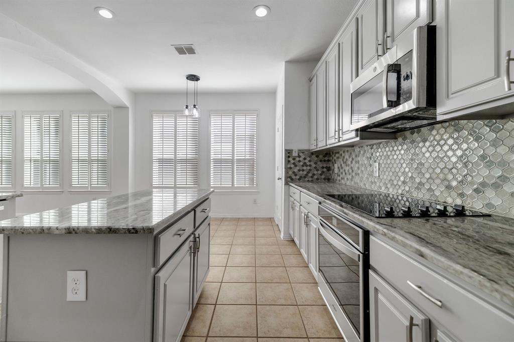 Kitchen featuring light-toned cabinetry, a stainless steel microwave, a built-in cooktop, and a distinct mosaic tile backsplash Kitchen featuring light-toned cabinetry, a stainless steel microwave, a built-in cooktop, and a distinct mosaic tile backsplash